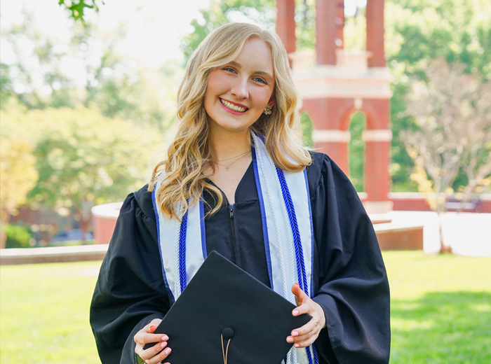 Young woman wearing graduation gown and holding graduation cap