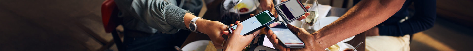 People holding cell phones together at dinner table