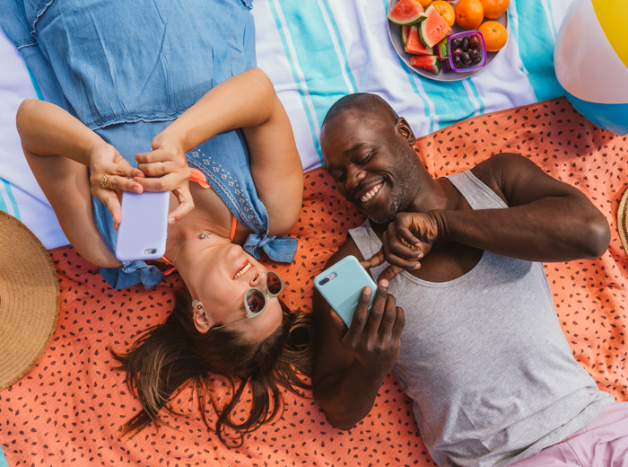 Man and woman lying on beach blanket holding cell phones