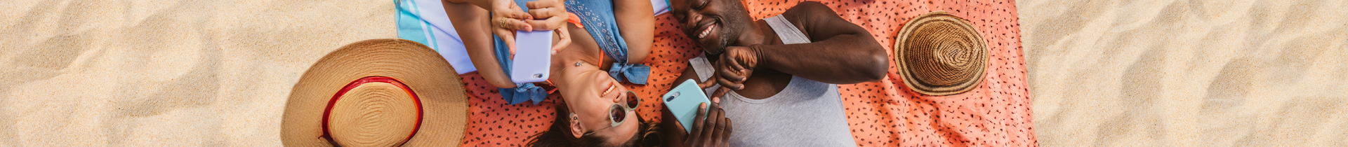 Man and woman lying on beach blanket holding cell phones